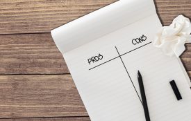 用黑色毛毡笔尖和一张皱皱的纸孤立在质朴的木桌背景上的规则记事本与字利弊