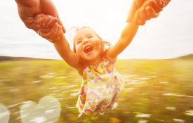 Happy girl spinning around her parent in a field.