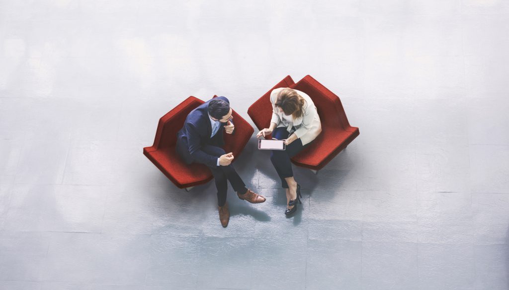 一名商人和一名女商人坐在办公楼大厅里使用平板电脑的高角度照片