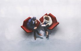 一个商人和一个女商人坐在办公大楼的大厅里，使用平板电脑的高角度视角