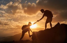 男女徒步者爬上悬崖，其中一人伸出援助之手。