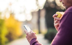 这是一张男人在户外一边吃苹果一边玩手机的照片。
