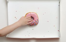 俯瞰甜甜圈盒，一个年轻女孩的手伸向最后一个粉红色草莓糖霜甜甜圈。