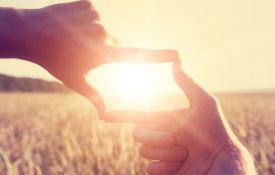 This is a photo of a woman using her hands to frame distant sun rays
